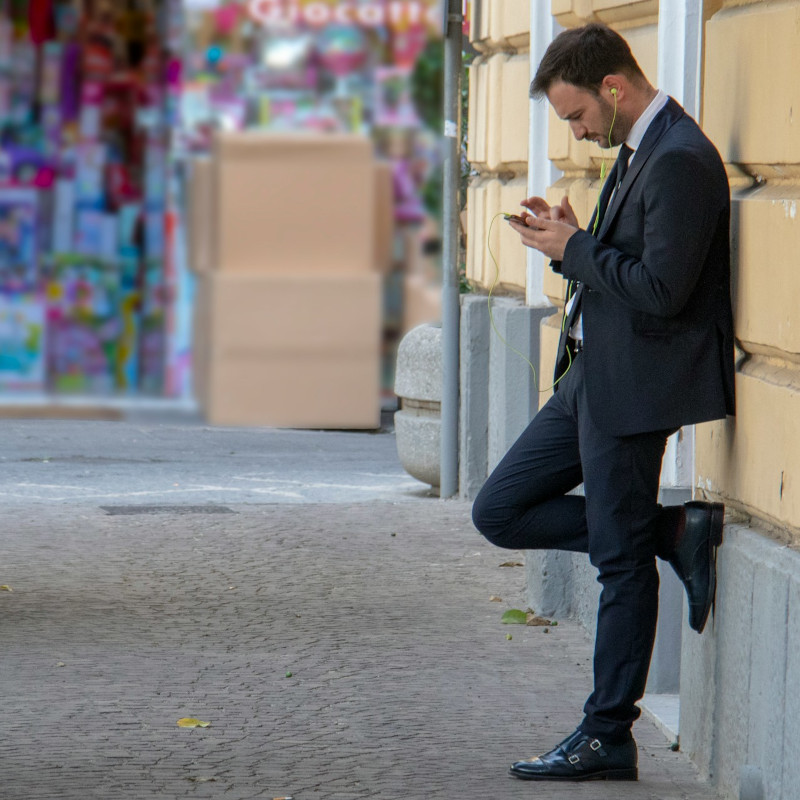 Man in a business suit leaning against a wall while using his smartphone.